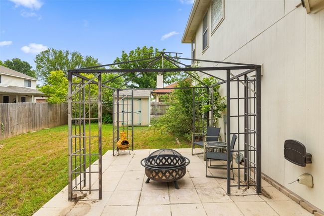 View of patio with a storage unit, a fenced backyard, a fire pit, and an outdoor structure | Image 37