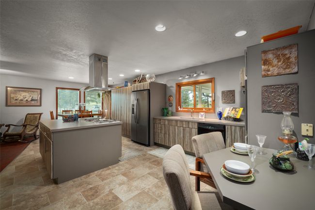 Kitchen featuring island range hood, stainless steel fridge with ice dispenser, a sink, light stone finish floors, and a textured ceiling | Image 22