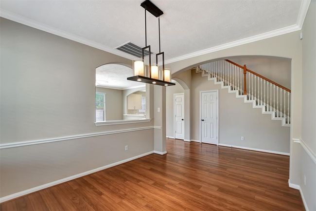 This spacious, well-lit area features warm wood flooring, neutral walls, and a modern chandelier. The open floor plan includes an elegant staircase and access to a kitchen through a stylish archway. Perfect for entertaining and daily living. | Image 11