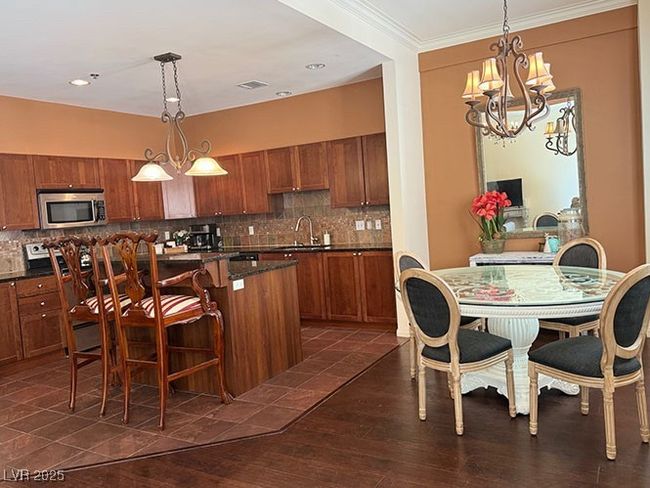 Kitchen featuring stainless steel microwave, brown cabinetry, dark countertops, a center island, and ornamental molding | Image 6