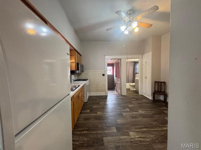 Kitchen with white appliances, ceiling fan, dark wood-style floors, brown cabinets, and light countertops | Image 13