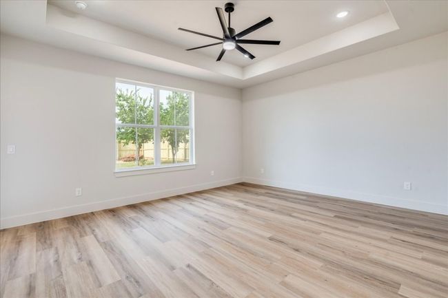 Empty room with a tray ceiling, light wood-type flooring, ceiling fan, and recessed lighting | Image 15