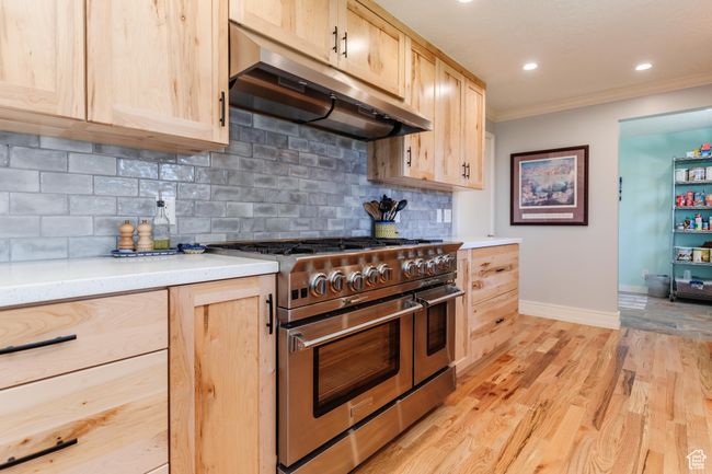 Kitchen with under cabinet range hood, light brown cabinetry, double oven range, baseboards, and ornamental molding | Image 10