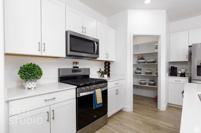 Kitchen featuring light wood-style floors, stainless steel appliances, light countertops, and white cabinets | Image 14