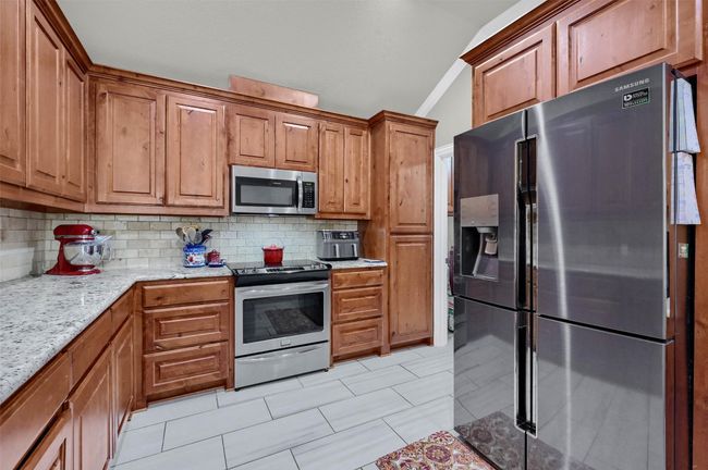 Kitchen featuring decorative backsplash, light stone counters, brown cabinetry, and appliances with stainless steel finishes | Image 14