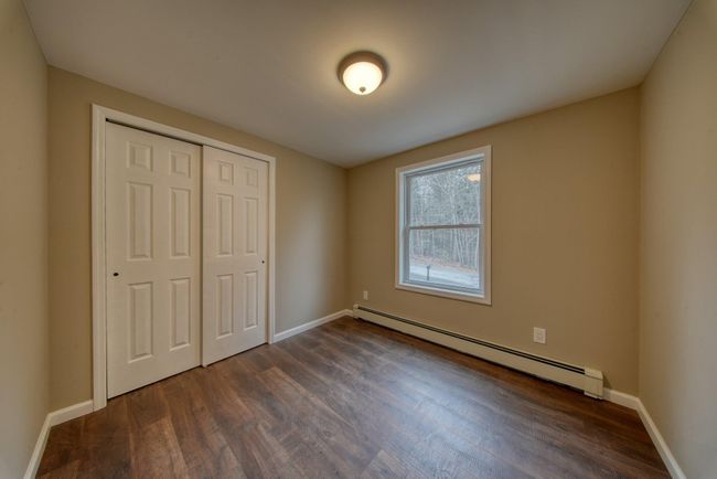 Unfurnished bedroom with a baseboard heating unit, baseboards, a closet, and dark wood-style flooring | Image 24
