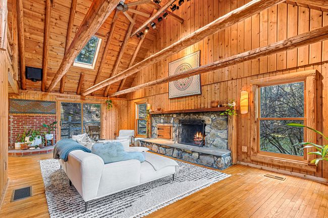Living room with high vaulted ceiling, wood walls, a stone fireplace, plenty of natural light, and hardwood / wood-style floors | Image 28