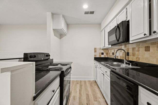 Your galley style kitchen features all black appliances, granite countertops, freshly painted cabinetry, new cabinet hardware, and tile backsplash. | Image 5