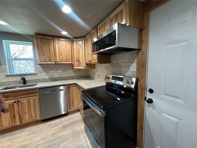 Kitchen featuring light stone countertops, tasteful backsplash, appliances with stainless steel finishes, a sink, and light wood-type flooring | Image 14