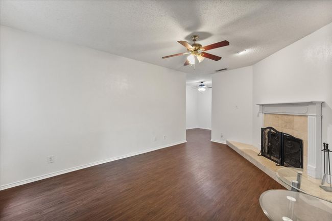Unfurnished living room with wood finished floors, ceiling fan, a tile fireplace, and a textured ceiling | Image 7