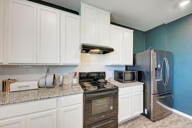 Kitchen with appliances with stainless steel finishes, under cabinet range hood, a textured wall, backsplash, and white cabinets | Image 20