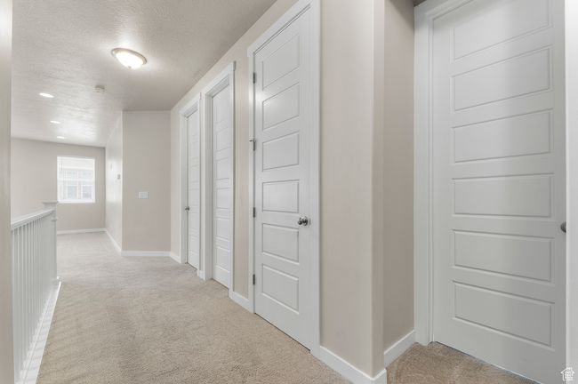Hallway featuring a textured ceiling, light colored carpet, and baseboards | Image 5