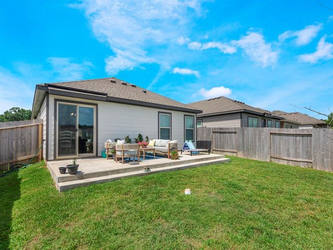 This photo showcases a fenced backyard with an oversized patio area featuring outdoor seating. The house has sliding glass doors leading to the patio, offering a space for relaxation and entertainment. The lawn is well-maintained, providing a pleasant outdoor environment. | Image 19