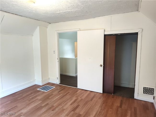 Unfurnished bedroom with wood finished floors, vaulted ceiling, a closet, a textured ceiling, and baseboards | Image 41