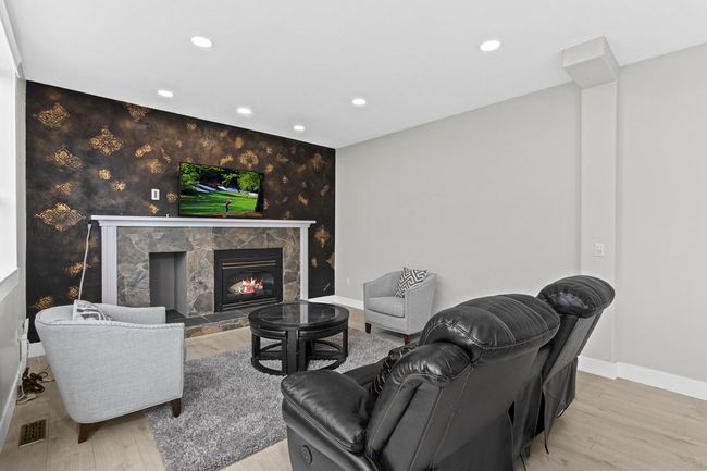 Living area with wood finished floors, a stone fireplace, visible vents, and recessed lighting | Image 16
