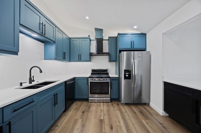 Kitchen with appliances with stainless steel finishes, wall chimney range hood, blue cabinetry, light wood finished floors, and recessed lighting | Image 9