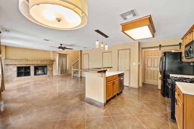 Kitchen with black range with gas cooktop, a barn door, ceiling fan, a kitchen island, and light countertops | Image 14