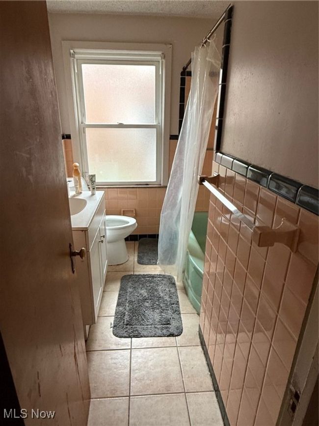 Bathroom with toilet, tile patterned floors, tile walls, and a textured ceiling | Image 8