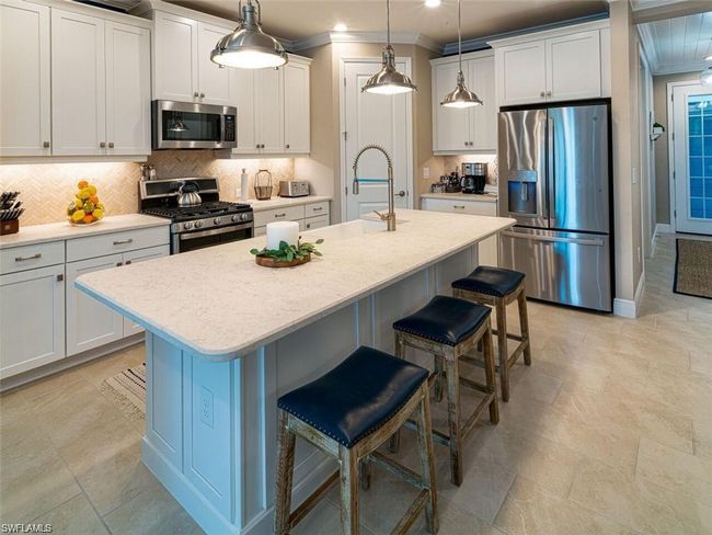 Kitchen with a center island with sink, white cabinetry, pendant lighting, and appliances with stainless steel finishes | Image 4