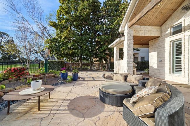 This photo showcases a spacious and inviting backyard patio with stylish stone flooring, and lush greenery. The area is perfect for relaxing or entertaining, offering a blend of natural beauty and modern comfort. | Image 36