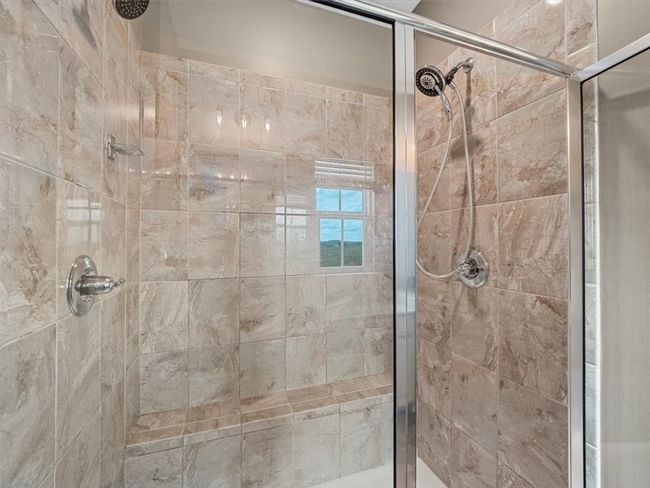 This luxurious walk-in shower showcases elegant floor-to-ceiling tile with rich, natural stone patterns that add warmth and sophistication. Featuring dual showerheads and sleek glass doors, the design offers both functionality and style. | Image 17