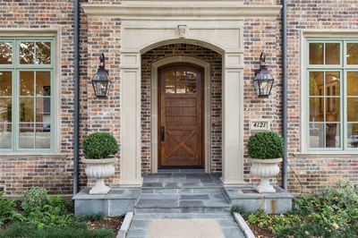 The wide eyebrow arched porch entry is accentuated by a hefty stone surround which is mimicked by the oversized front door. Great design. Even the porch and sidewalk are finished...no plain concrete here! | Image 2