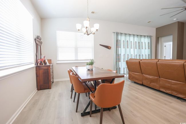 Dining space with light wood finished floors, visible vents, baseboards, vaulted ceiling, and ceiling fan with notable chandelier | Image 16