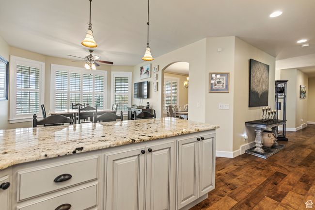 Kitchen with white cabinets, dark hardwood / wood-style floors, ceiling fan, light stone countertops, and decorative light fixtures | Image 37