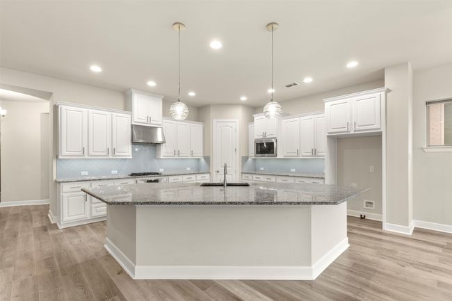 Kitchen featuring stainless steel microwave, under cabinet range hood, an island with sink, white cabinetry, and recessed lighting | Image 5