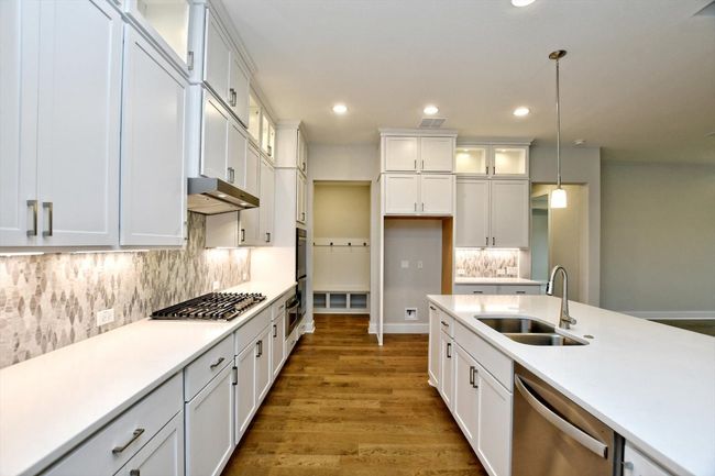 Kitchen featuring stainless steel appliances, under cabinet range hood, hanging light fixtures, a sink, and white cabinets | Image 12
