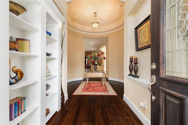 Step inside to a stunning, curved entry with tray ceiling and real wood floors. A surprise awaits just behind the custom-built bookshelves. | Image 4