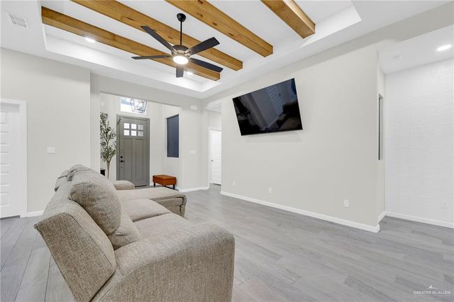 Living room with visible vents, wood-style tile flooring, beamed ceiling, a raised ceiling, and a ceiling fan | Image 9