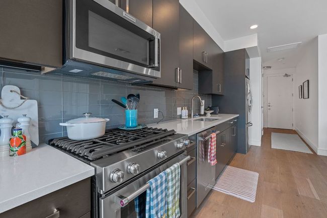 Kitchen featuring appliances with stainless steel finishes, a sink, light countertops, light wood-style flooring, and decorative backsplash | Image 5