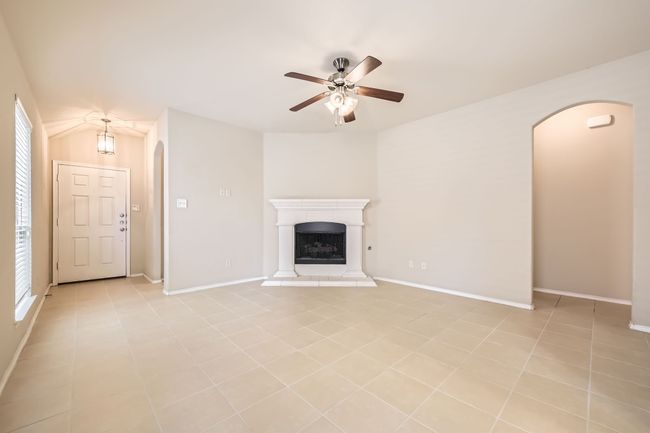 Unfurnished living room with arched walkways, ceiling fan, and a fireplace with raised hearth | Image 5