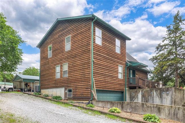 View of home's exterior featuring an attached garage, log veneer siding, and gravel driveway | Image 4