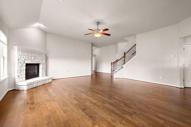 Unfurnished living room with stairs, hardwood / wood-style floors, ceiling fan, a fireplace, and baseboards | Image 6