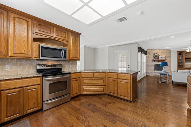 Kitchen featuring visible vents, ornamental molding, a fireplace, appliances with stainless steel finishes, and dark wood-style flooring | Image 10