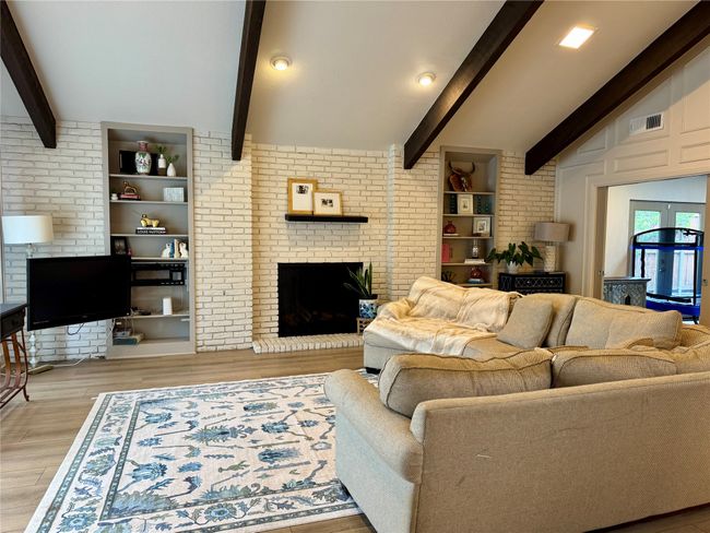 Living area with beam ceiling, brick wall and fireplace, luxury wide plank luxury vinyl floors | Image 6