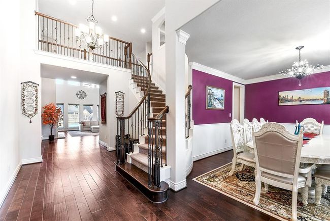 As you stand in the home office doorway, you'll be greeted by a beautiful view of the open space. To the right the elegant formal dining room awaits, offering a perfect setting for gatherings and meals. The impressive staircase with its intricate wrought iron design is a stunning focal point, adding a touch of sophistication to the home’s entryway. The same rich wood flooring flows seamlessly throughout the home and Crown molding is featured throughout. | Image 11