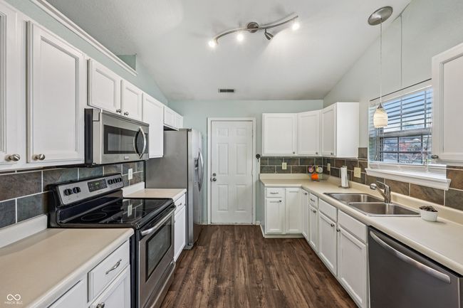 kitchen featuring stainless steel appliances, vaulted ceiling, white cabinets, light countertops, and tasteful backsplash | Image 16