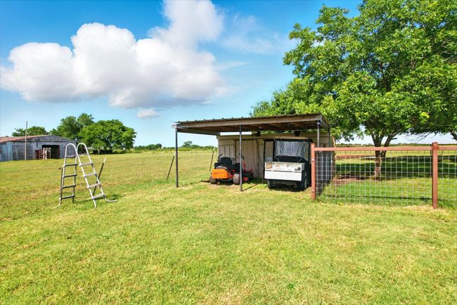 View of grassy yard featuring a detached carport and an outbuilding | Image 12