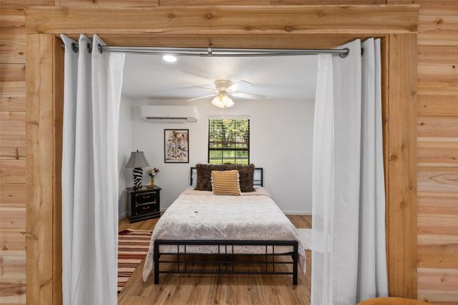 Bedroom featuring baseboards, a ceiling fan, wood finished floors, and a wall mounted air conditioner | Image 31