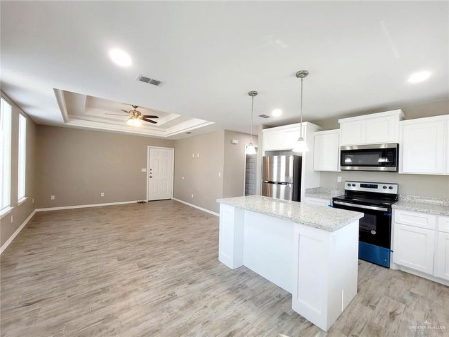 Kitchen featuring stainless steel appliances, a tray ceiling, a center island, ceiling fan, and white cabinetry | Image 9