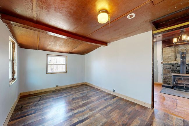 Unfurnished room with baseboards, vaulted ceiling with beams, wood finished floors, and a wood stove | Image 11