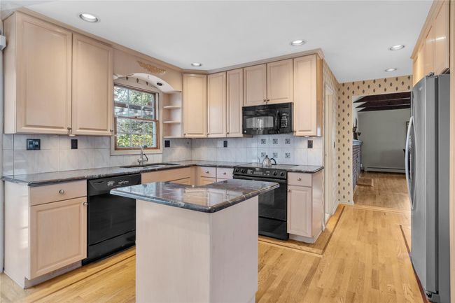 Kitchen with black appliances, light wood-style floors, a sink, and dark stone countertops | Image 7