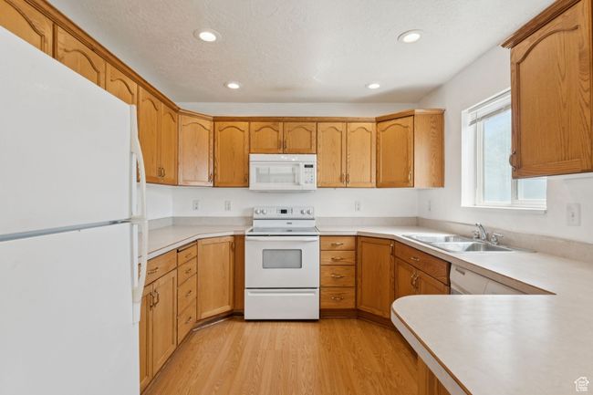 Kitchen with white appliances, light wood-type flooring, recessed lighting, light countertops, and brown cabinets | Image 6