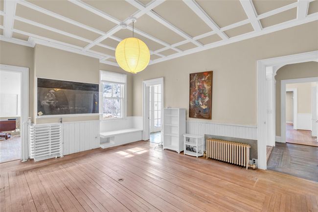Unfurnished living room with wainscoting, radiator heating unit, coffered ceiling, and wood finished floors | Image 12