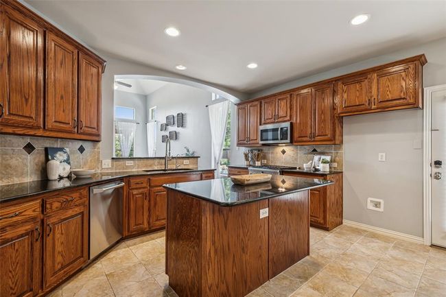 Kitchen featuring a kitchen island, tasteful backsplash, light tile floors, and stainless steel appliances | Image 7