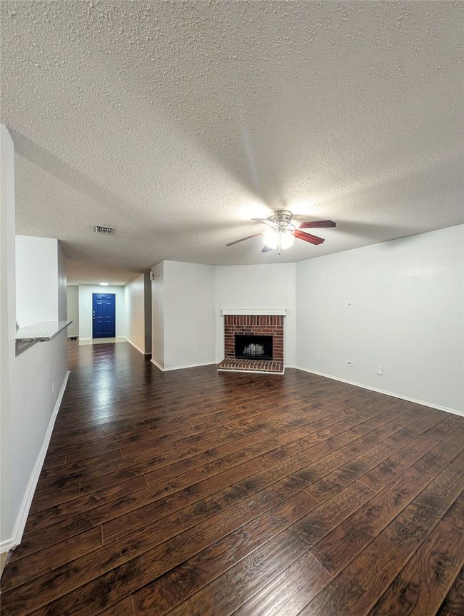 Unfurnished living room with dark wood-type flooring, a brick fireplace, a ceiling fan, baseboards, and a textured ceiling | Image 4