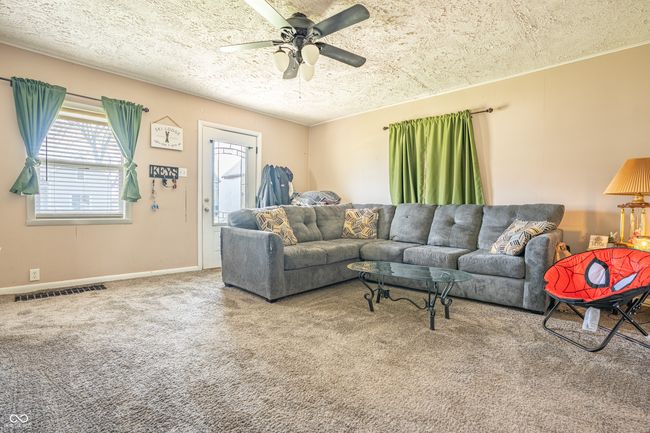 living room with carpet flooring, a textured ceiling, visible vents, baseboards, and a ceiling fan | Image 4